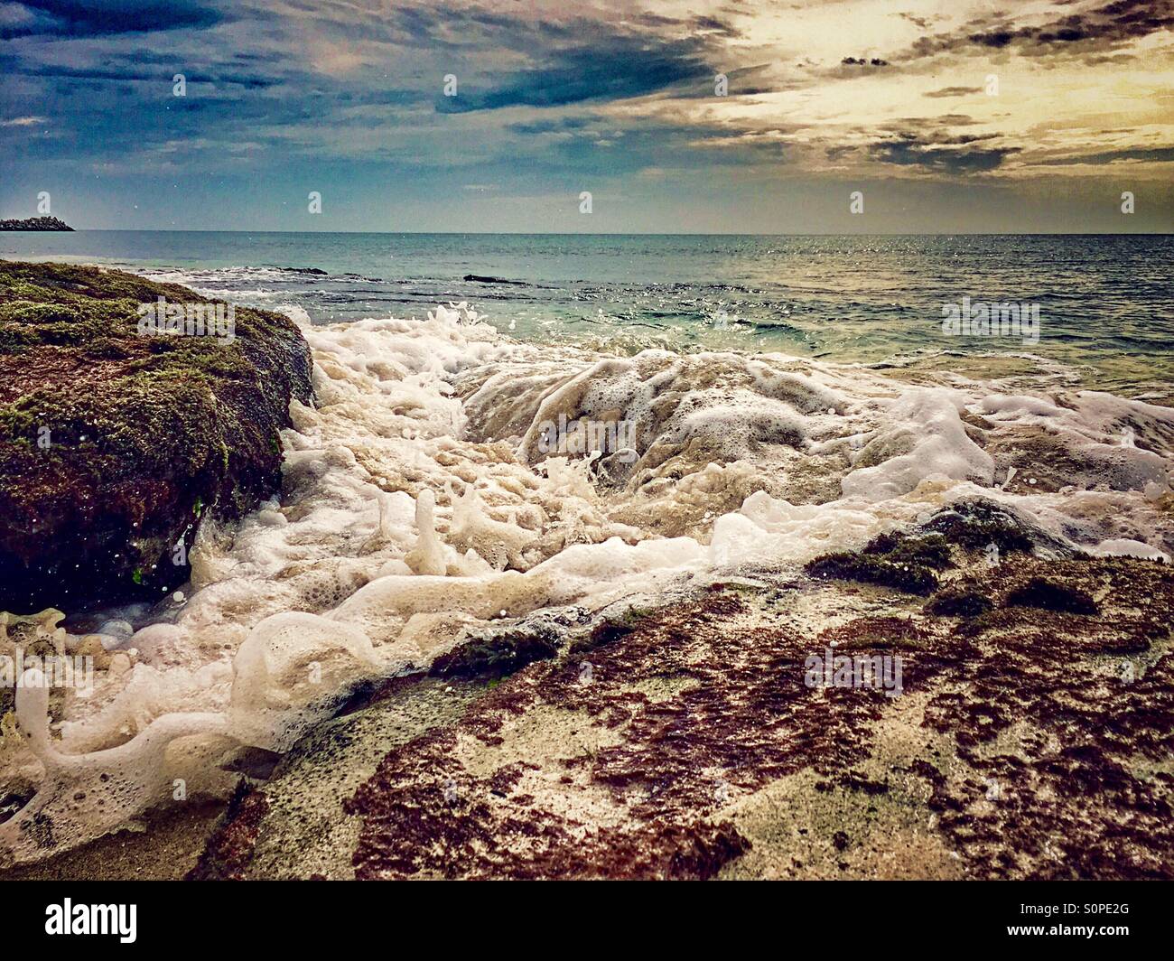 Incoming tide with water rushing past rocks on the beach - Smartphone Captured Stock Image