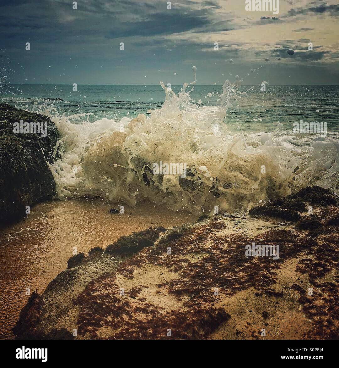 Dramatic grey sky as waves crash in between rocks on a sandy beach - Smartphone Captured Stock Image