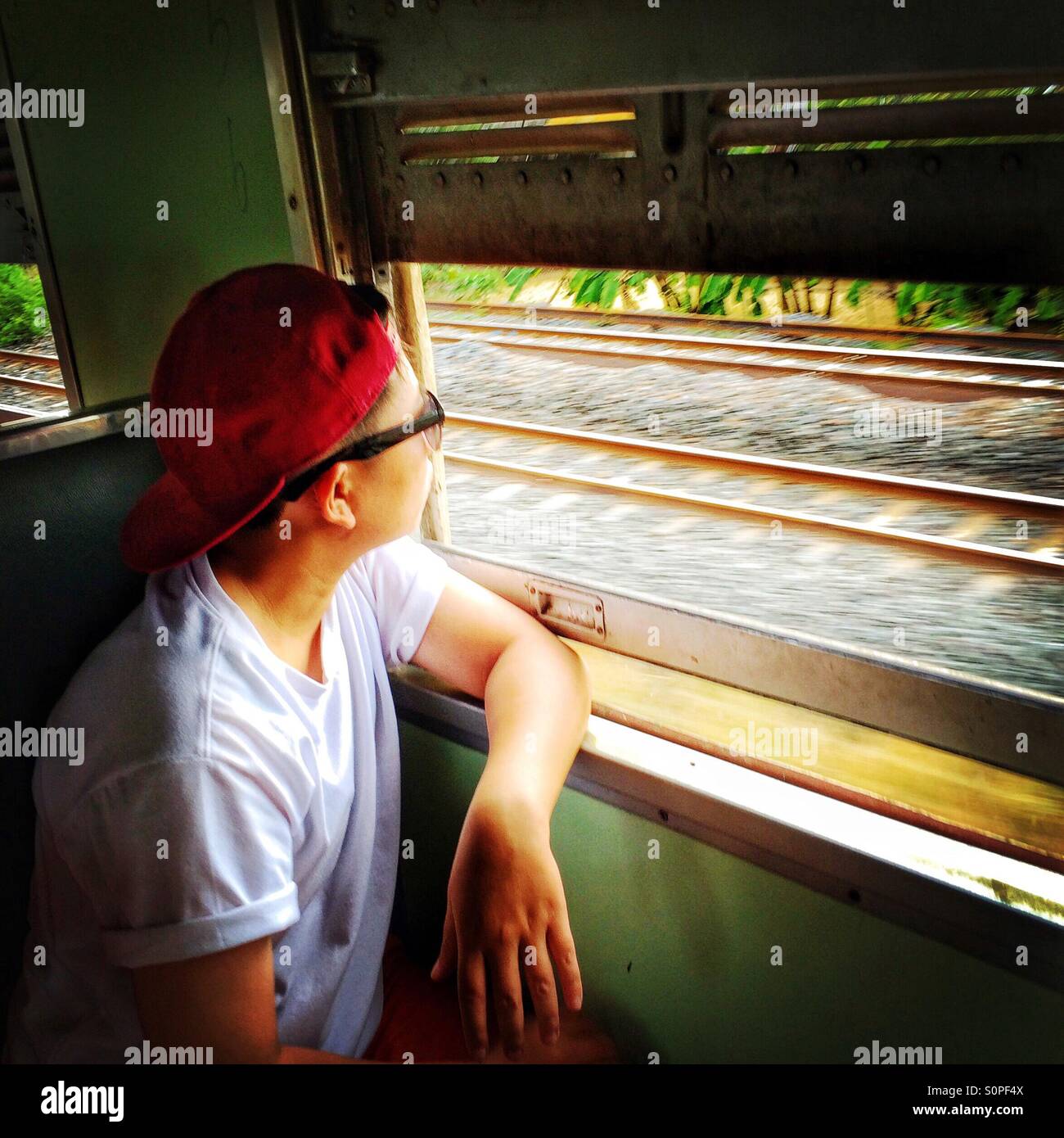 Passenger sitting by the window of a moving train in Bangkok, Thailand - Smartphone Captured Stock Image