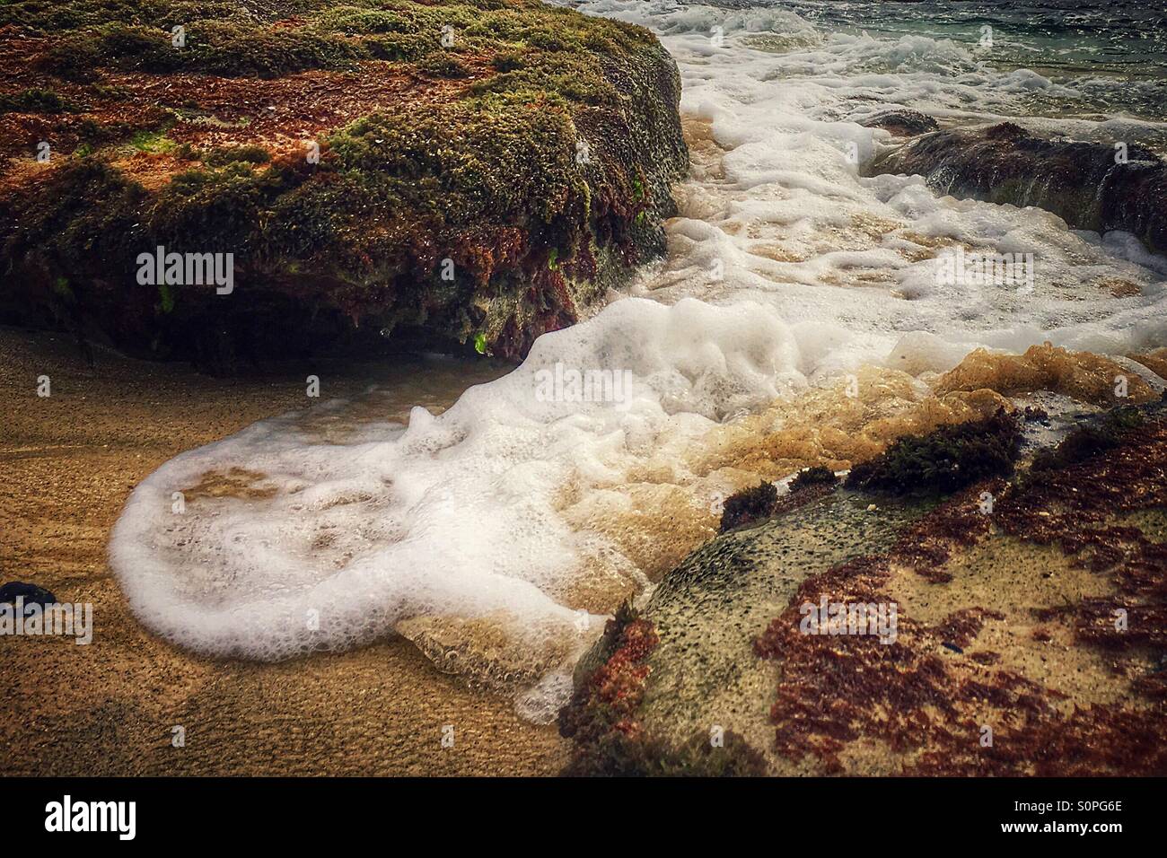 Foaming tide against rocks Stock Photo - Alamy