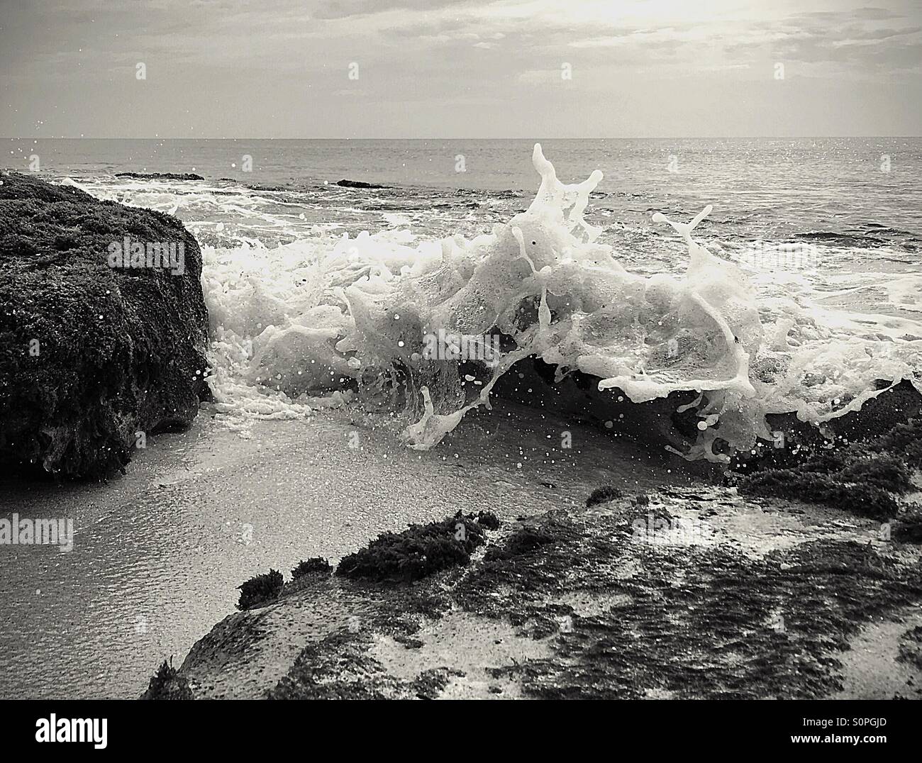 Black and white image of waves crashing over rocks - Smartphone Captured Stock Image