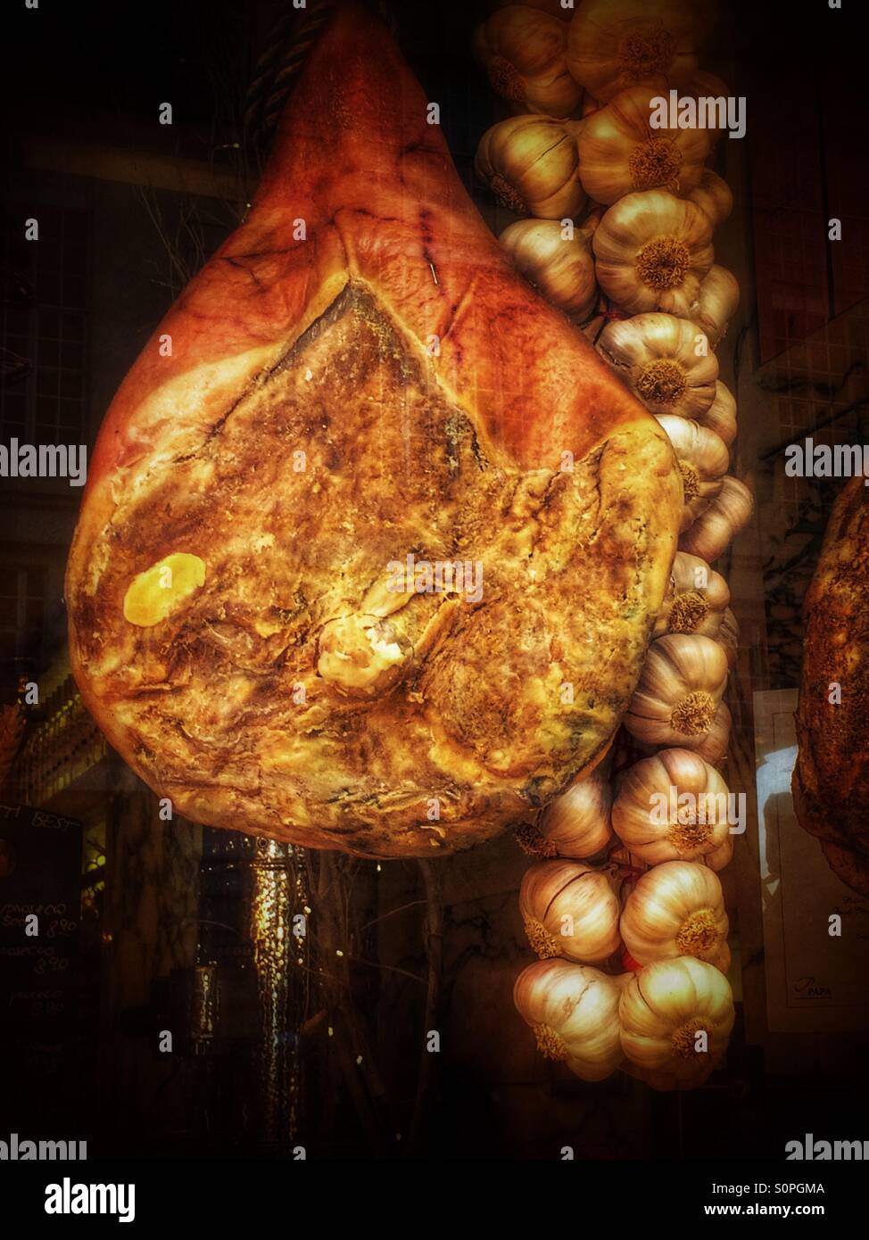 Cured ham and garlic string in a delicatessen's window. - Smartphone Captured Stock Image