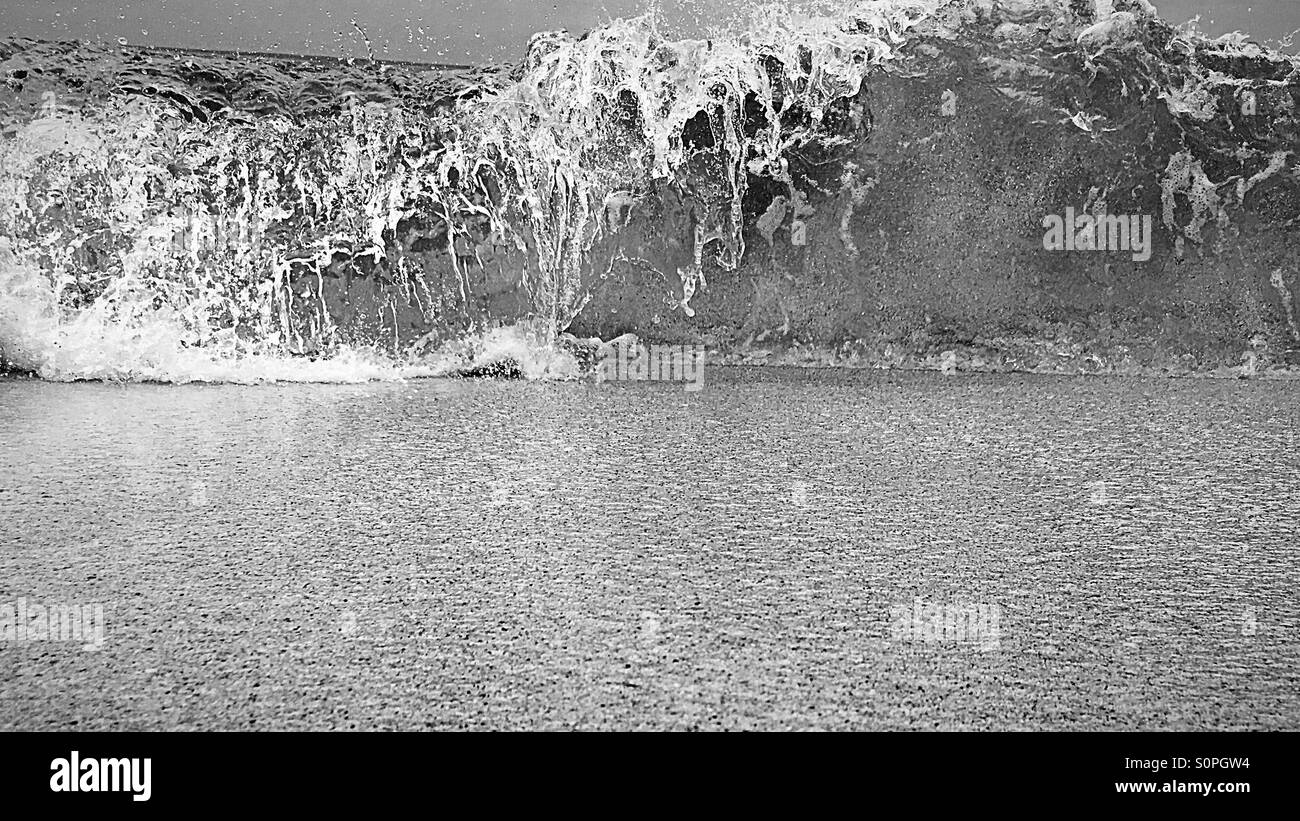 Wave breaking towards the camera on a sandy beach in black and white - Smartphone Captured Stock Image