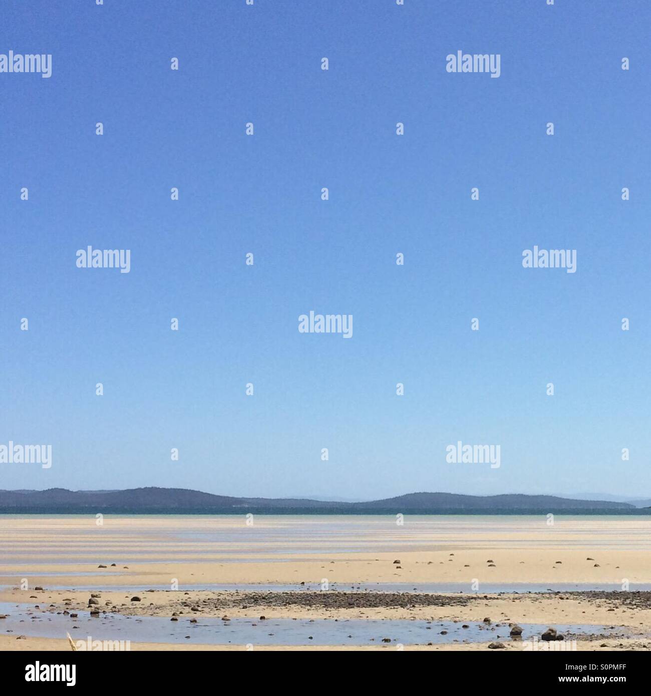 Sandy, low tide beach with blue skies in the background - Smartphone Captured Stock Image