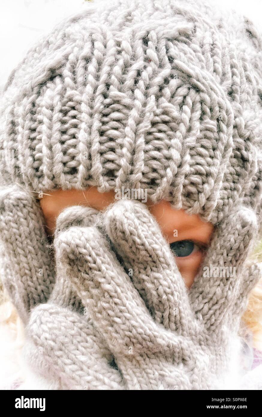 Young girl peeping out between gloved hands Stock Photo