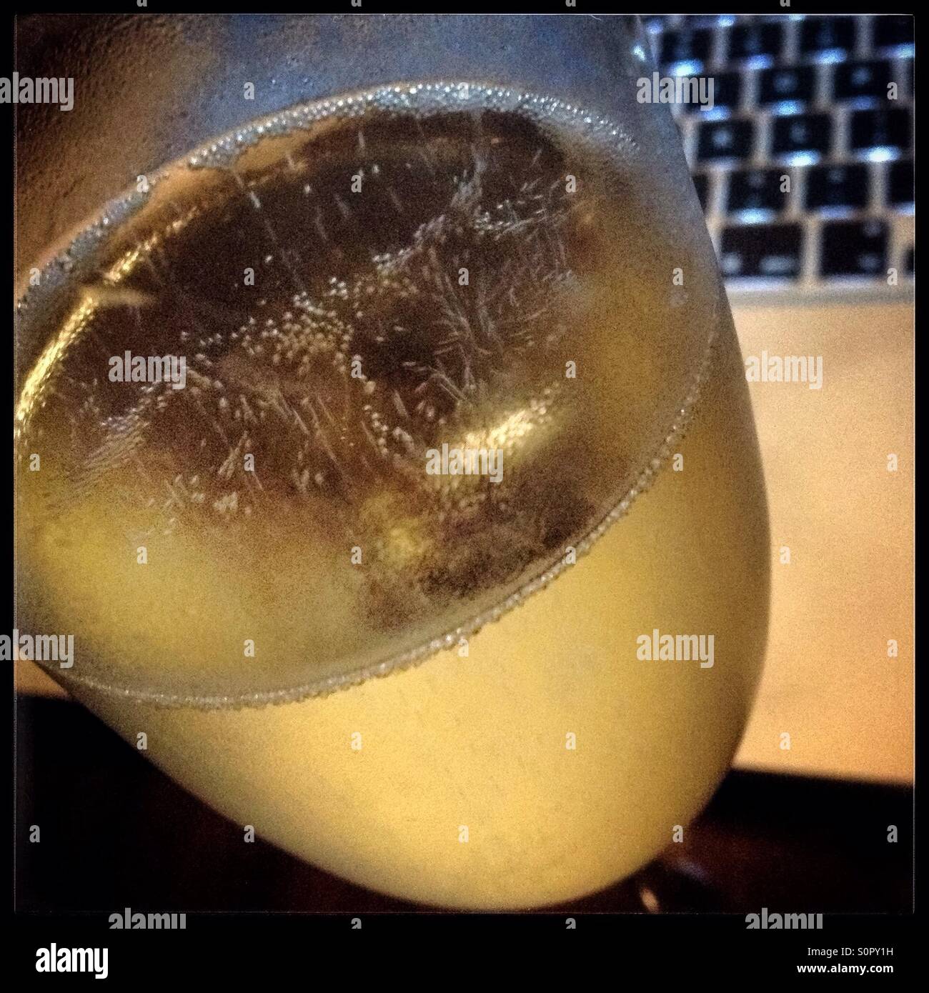 A glass of Cava sparkling wine with a computer in the background. - Smartphone Captured Stock Image