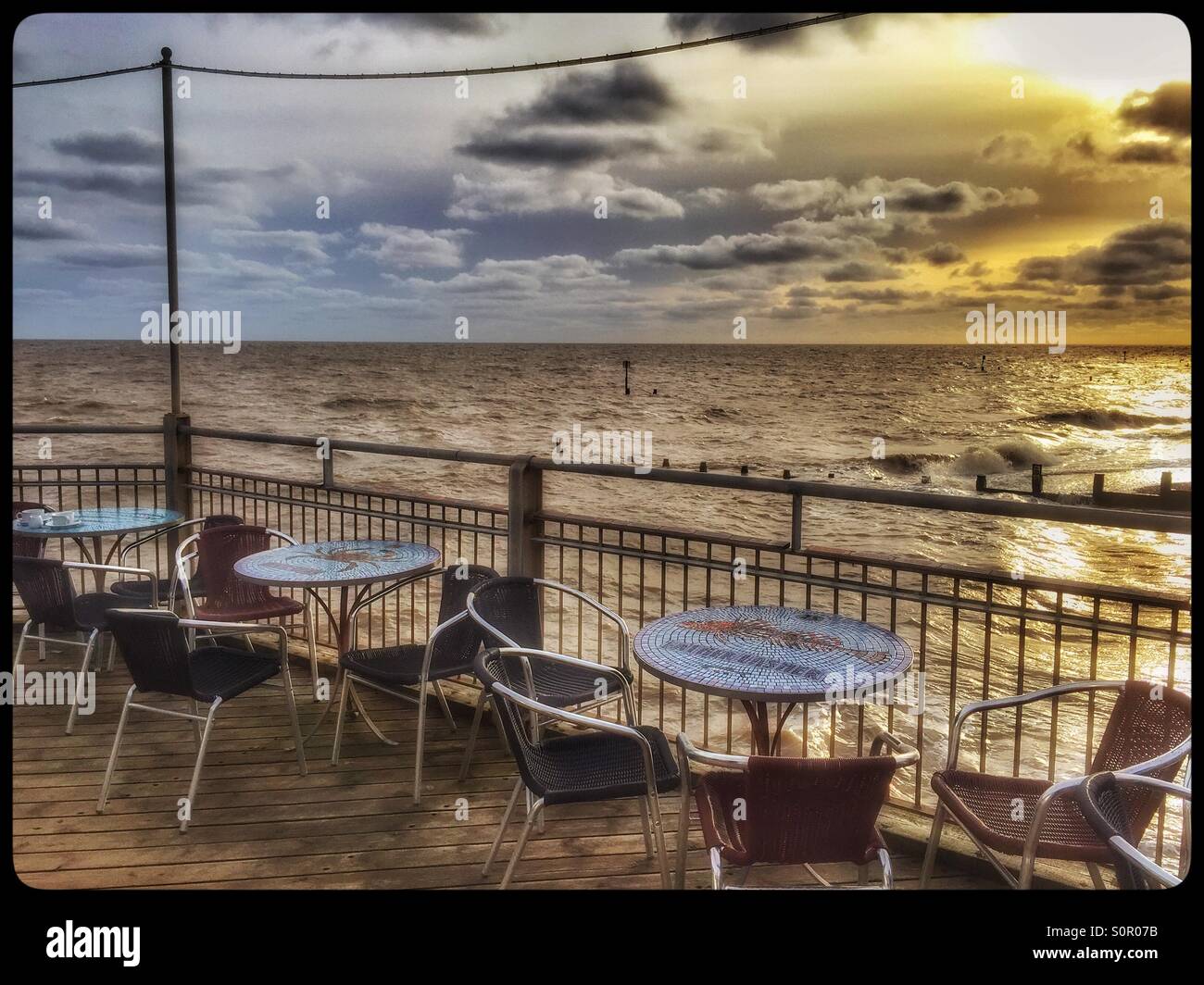 A winter view out to The North Sea from The Pier at Southwold, Suffolk, England. The sun is starting to set, and the tables and chairs have been abandoned. Photo Credit - © COLIN HOSKINS. - Smartphone Captured Stock Image