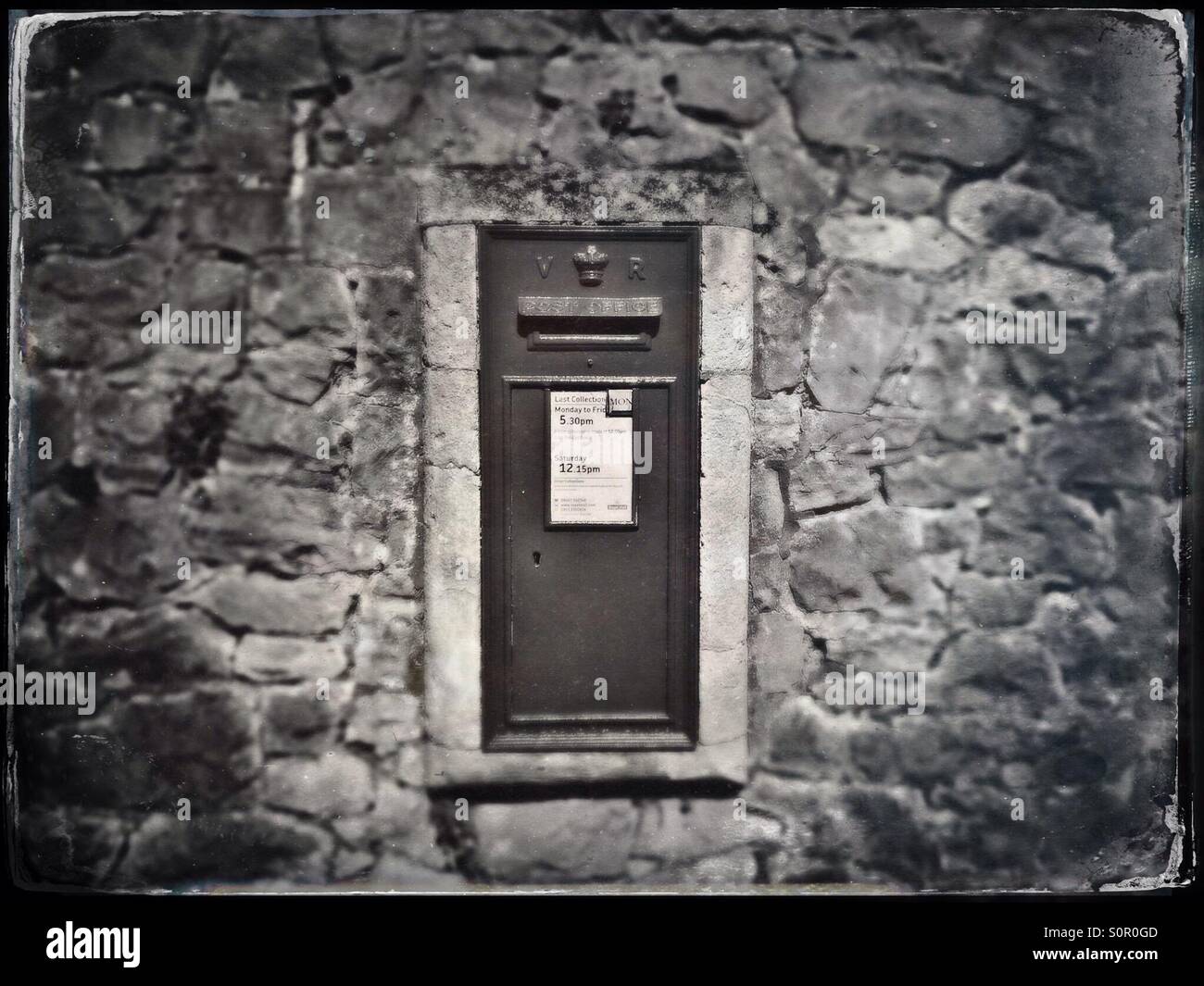 A faux tintype photograph of a Victorian post box set in a stone wall on a city street in England - Smartphone Captured Stock Image