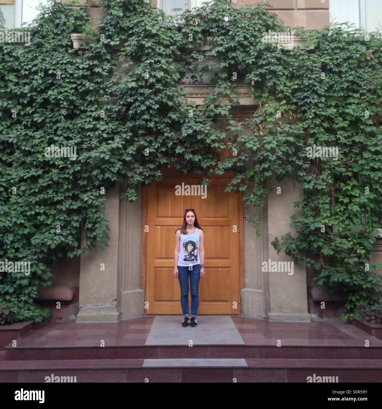 A girl stands facing the camera at the door of ivied buildings Stock Photo