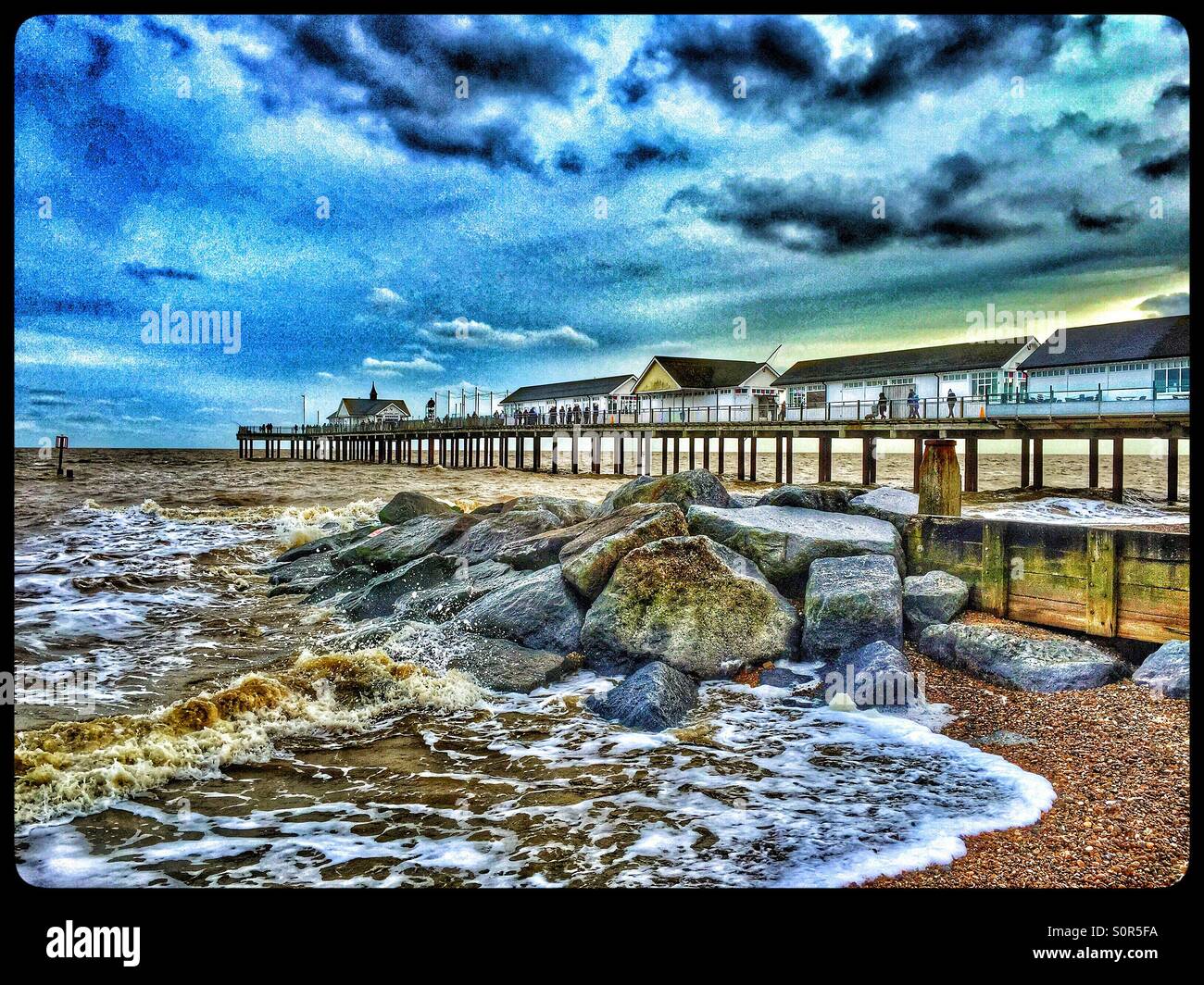An HDR view of Southwold Pier in January. Small waves the colour of dirty brown water, break over a group of rocks on the Beach. Photo Credit - © COLIN HOSKINS. - Smartphone Captured Stock Image