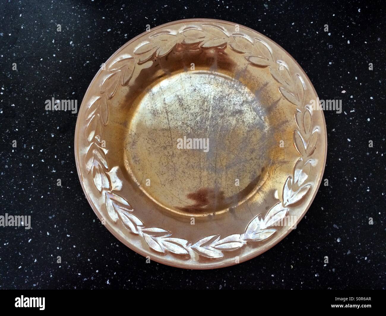 A decorative yellow plate with a worn scratched surface on a black counter top - Smartphone Captured Stock Image