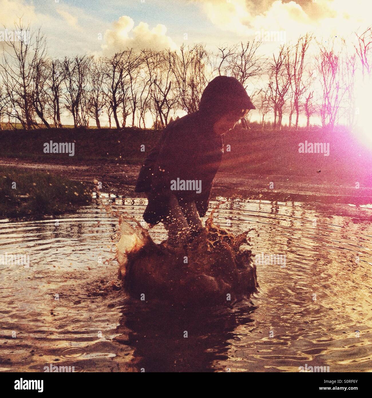 Six year old boy splashing in a muddy puddle! Hampshire, England, United Kingdom. - Smartphone Captured Stock Image