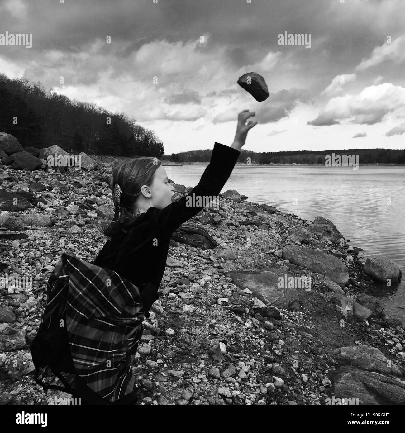 Girl tossing rock into lake Stock Photo