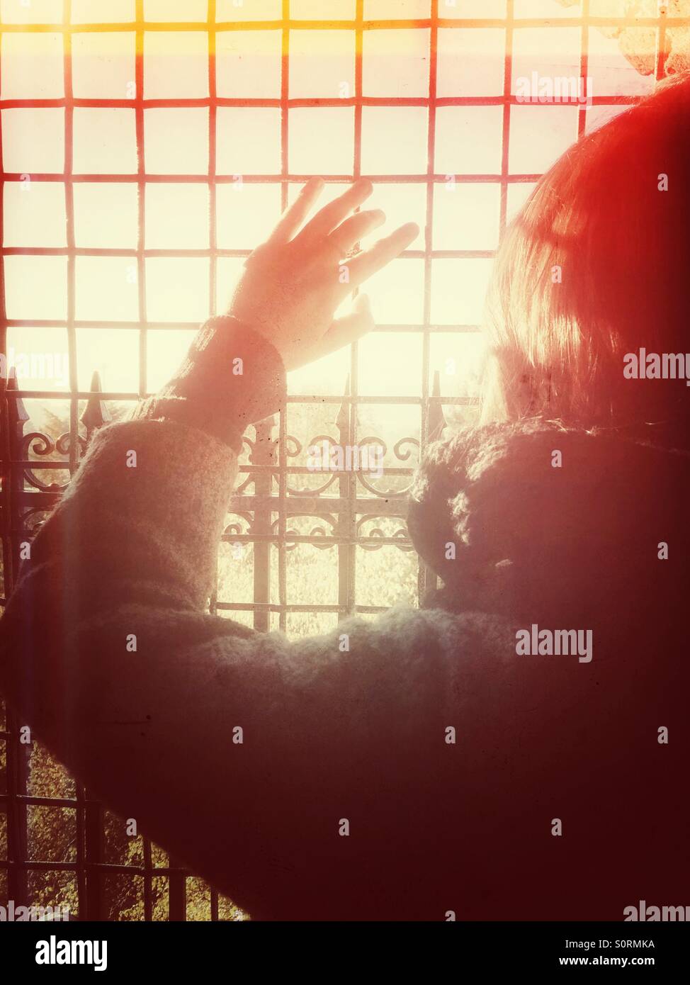 Girl holds hand up defensively against the sun shining through the metal grid - Smartphone Captured Stock Image Girl holds hand up defensively against the sun shining through the metal grid - Smartphone Captured Stock Image