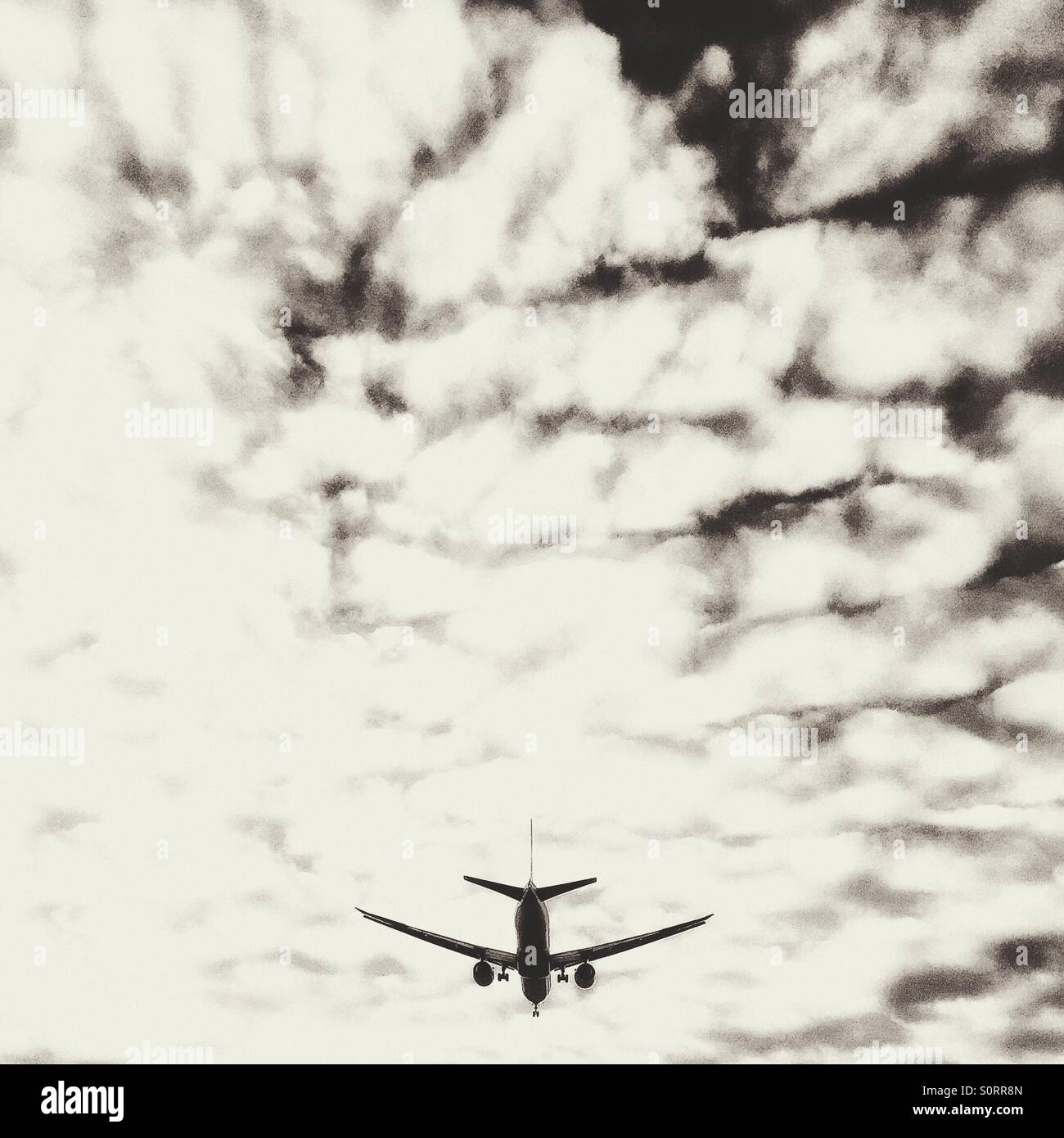 Airplane in the bright cloudy sky. Black and white. - Smartphone Captured Stock Image