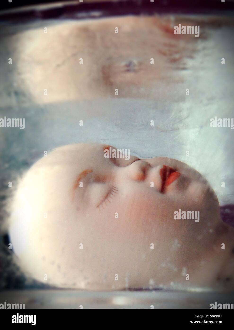 A surreal doll head frozen in ice. Stock Photo