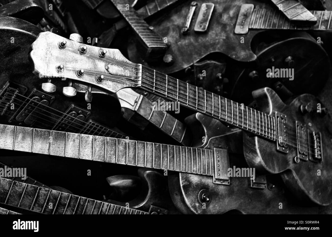 A pile of unused metallic guitars with a black and white, monochrome hue. Stock Photo