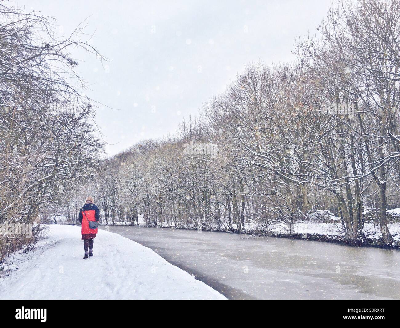 Lone woman in red coat walking along canal tow path in the snow - Smartphone Captured Stock Image