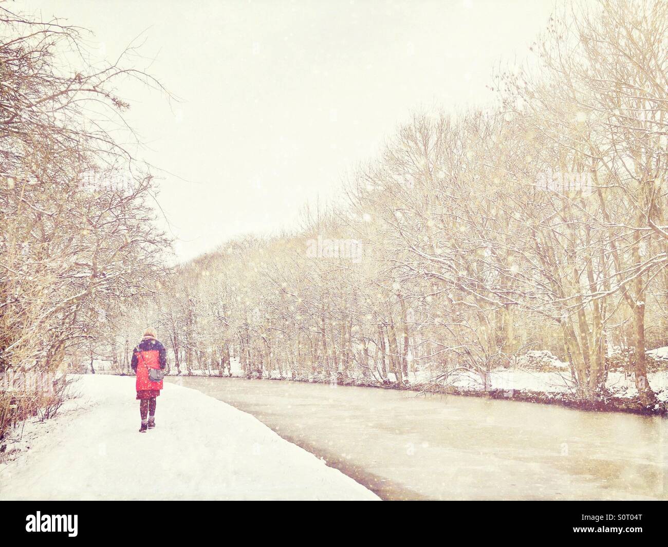 Woman in red coat walking along canal tow path in falling snow - Smartphone Captured Stock Image