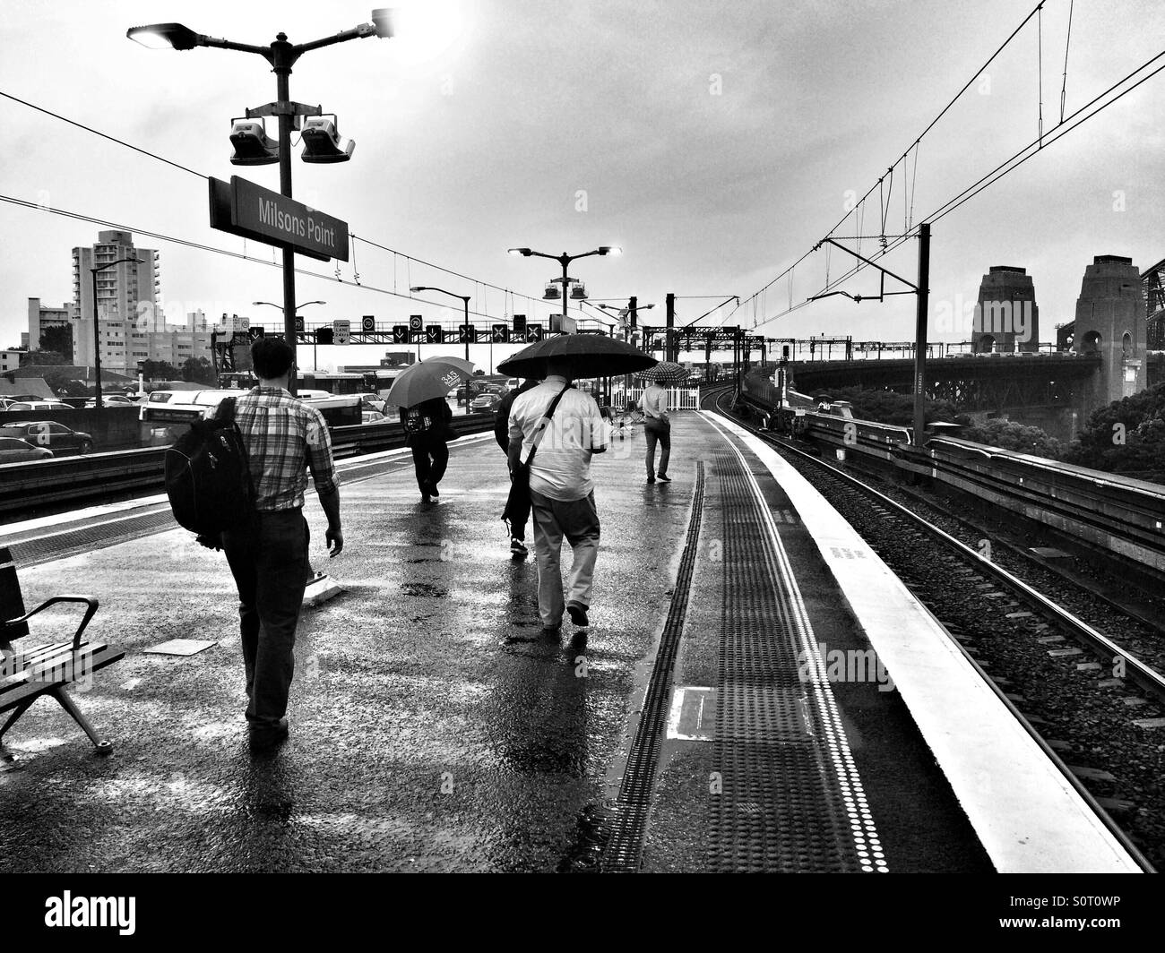 Passengers walk out into the rain on Milsons Point station near the Sydney Harbour Bridge on a rainy Friday evening - Smartphone Captured Stock Image