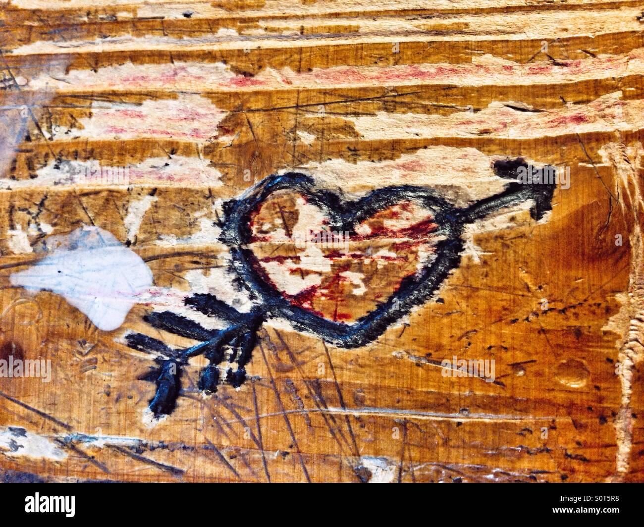 A heart pierced with an arrow carved into the surface of a wooden table - Smartphone Captured Stock Image