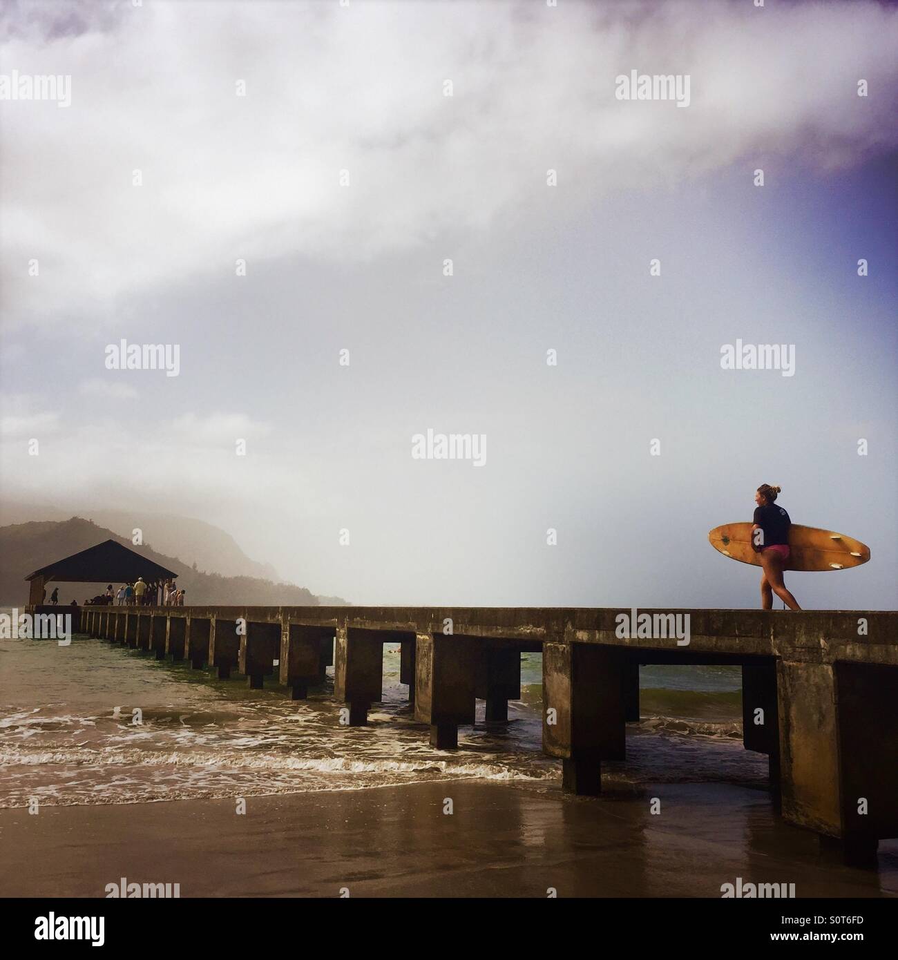 A female surfer walks on the Hanalei pier. Hanalei, Kauai USA. - Smartphone Captured Stock Image