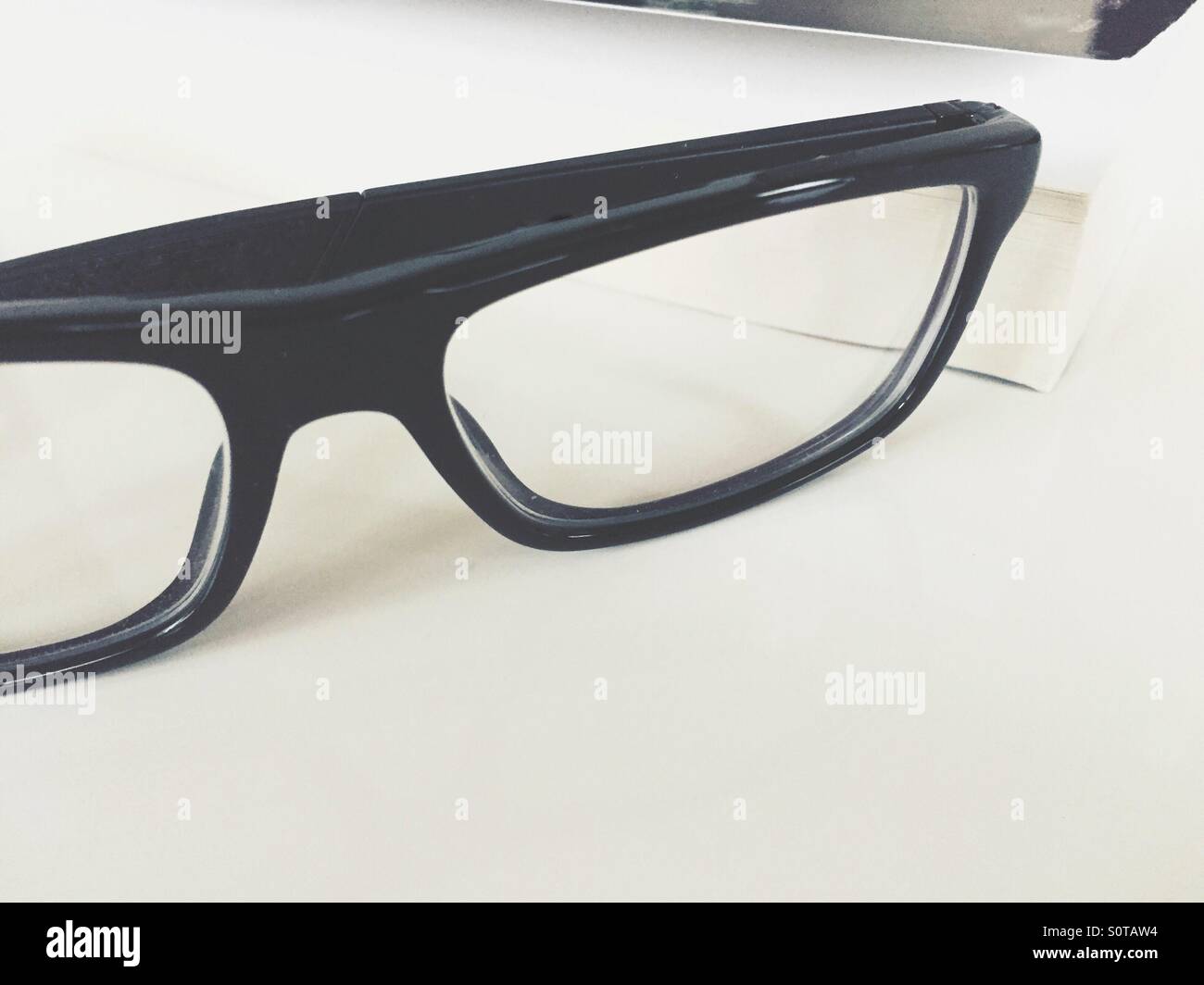 Prescription glasses and a book on a white table. - Smartphone Captured Stock Image