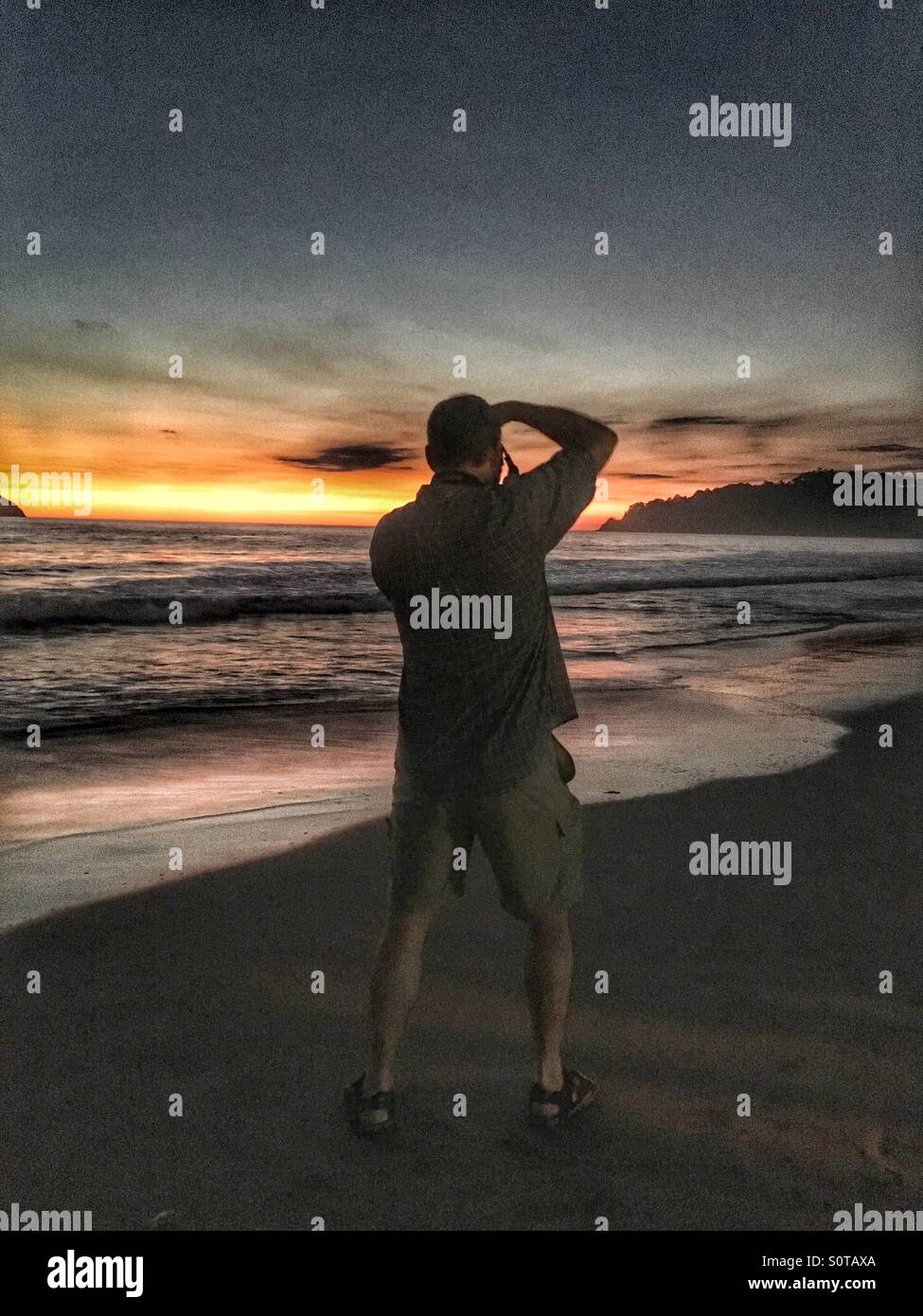 Man taking photograph of Costa Rican beach at sunset - Smartphone Captured Stock Image