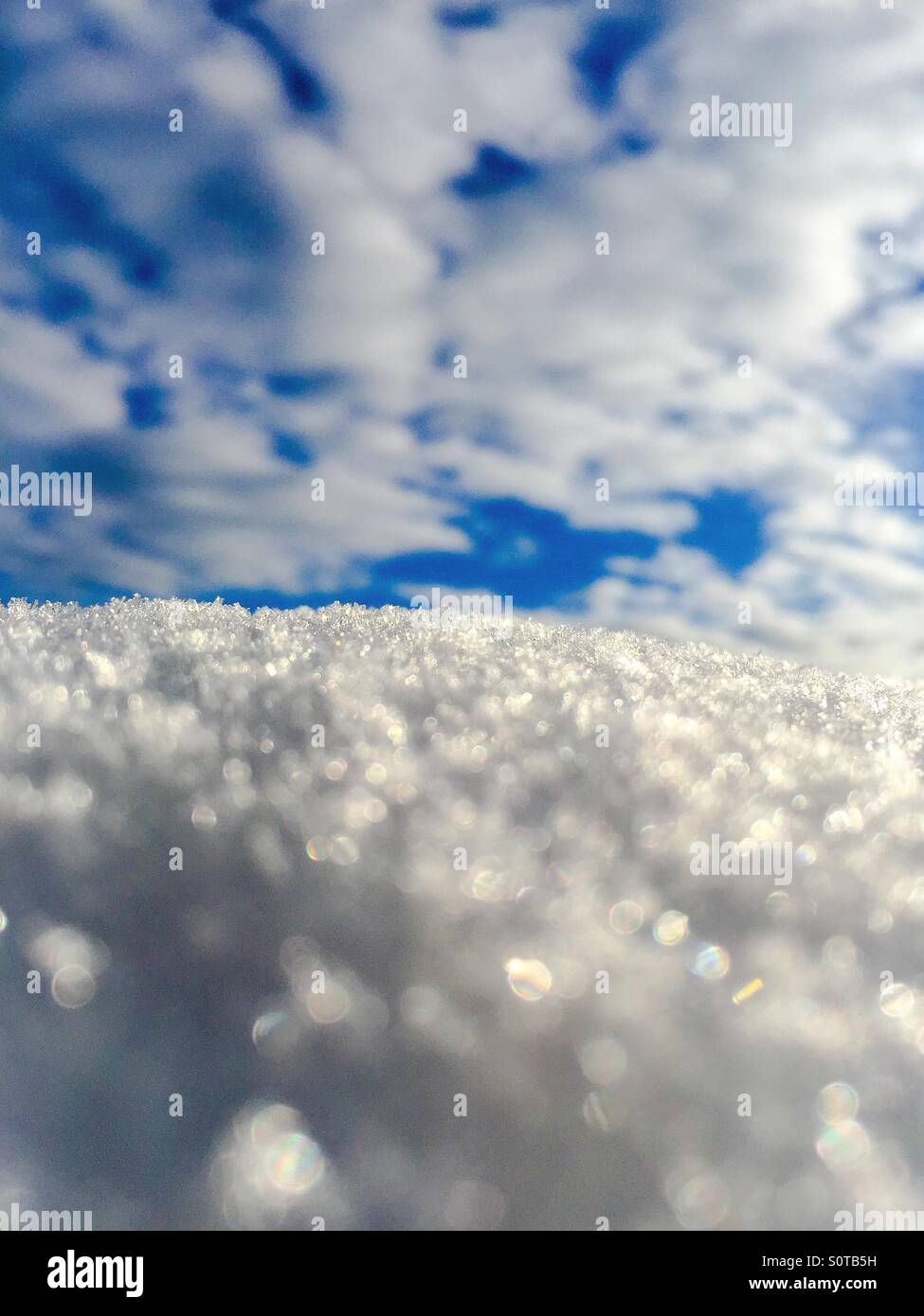 Close up of sparkling snow with blue skies and white clouds above. - Smartphone Captured Stock Image