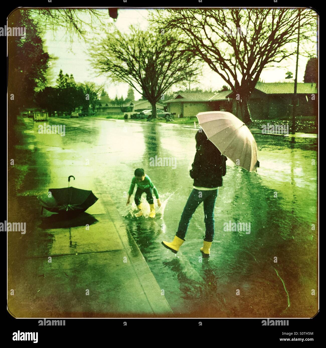 A 12 year old girl and her 7 year old brother play outside in the rain. - Smartphone Captured Stock Image