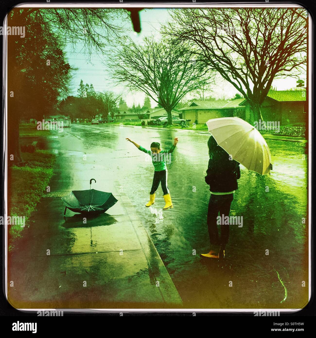 A 12 year old girl and her 7 year old brother play outside in the rain. - Smartphone Captured Stock Image