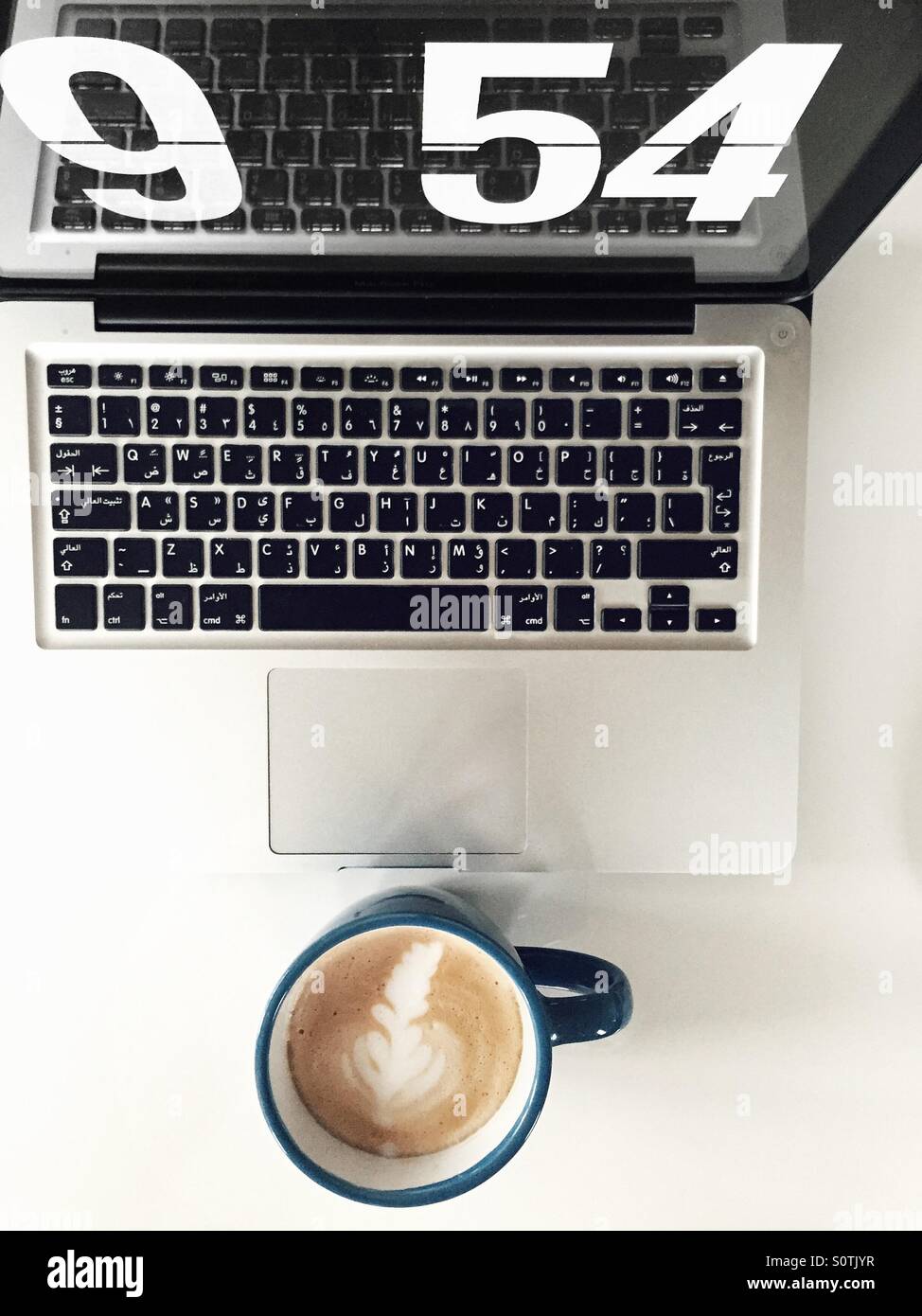Cup of latte & a laptop with clock screen saver and arabic keyboard. - Smartphone Captured Stock Image