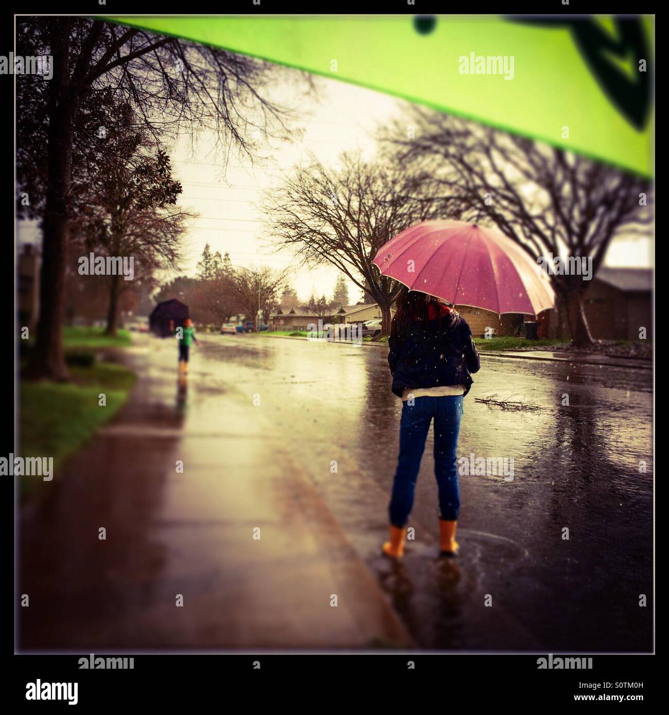 A 12 year old girl and her 7 year old brother play outside in the rain. - Smartphone Captured Stock Image