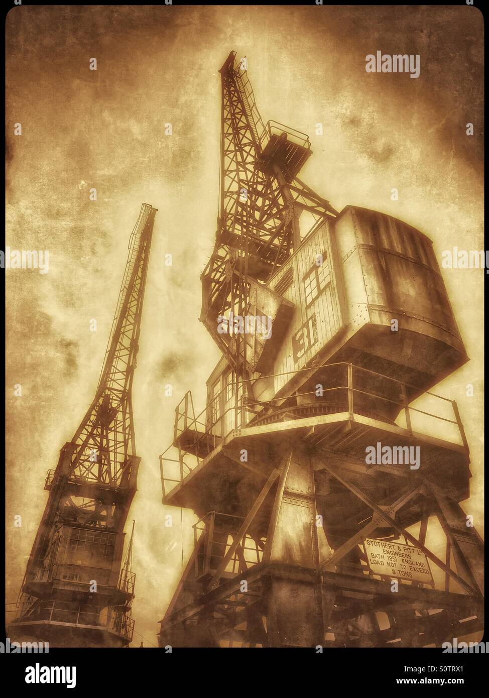 A Sepia Antique Effect Picture of Two Cranes that are situated on the edge of The Floating Harbour, close to the City Centre of Bristol, England, UK. Photo Credit - © COLIN HOSKINS. - Smartphone Captured Stock Image