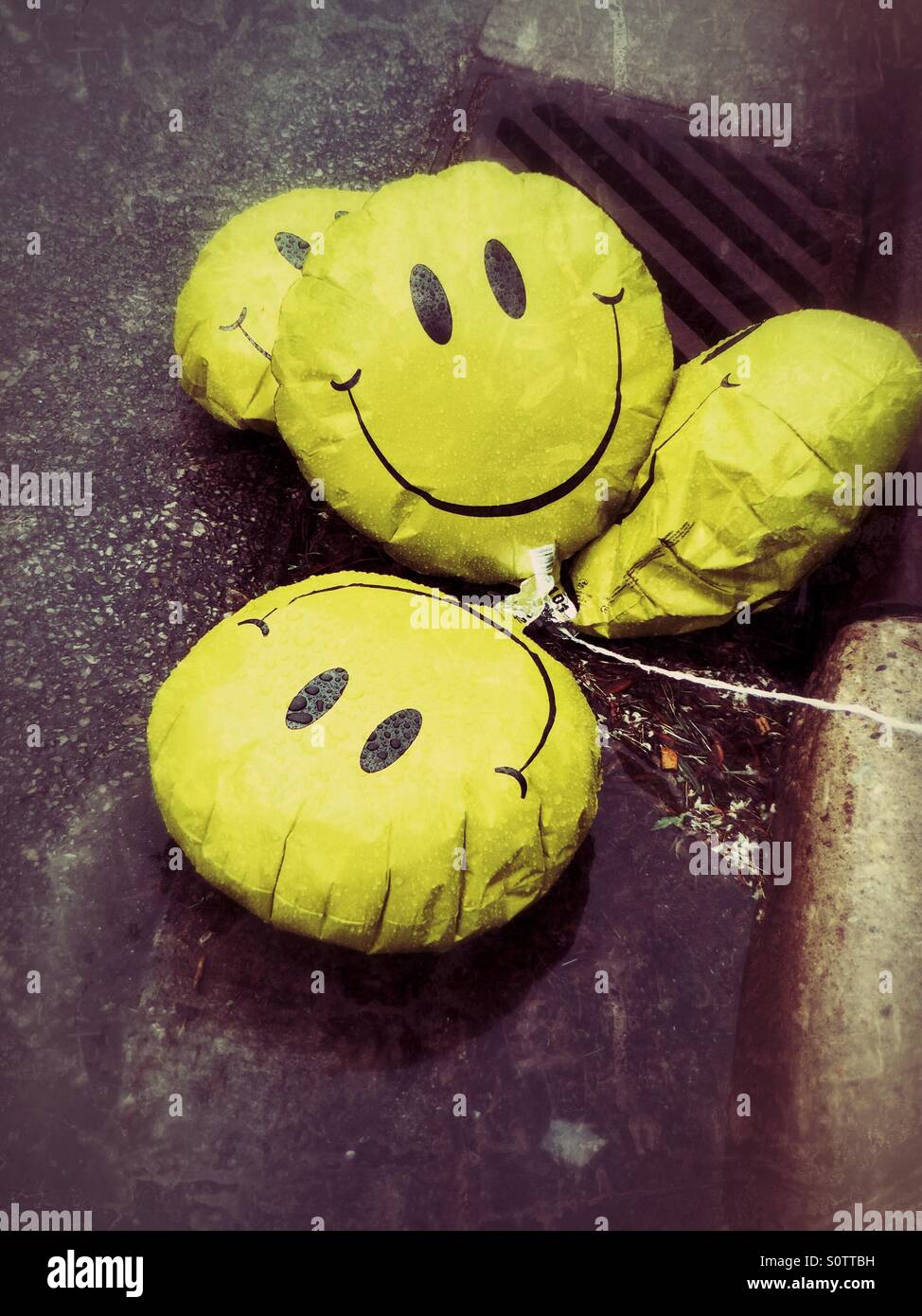 Sad, deflated happy face balloons laying in a puddle on the side of the street Stock Photo