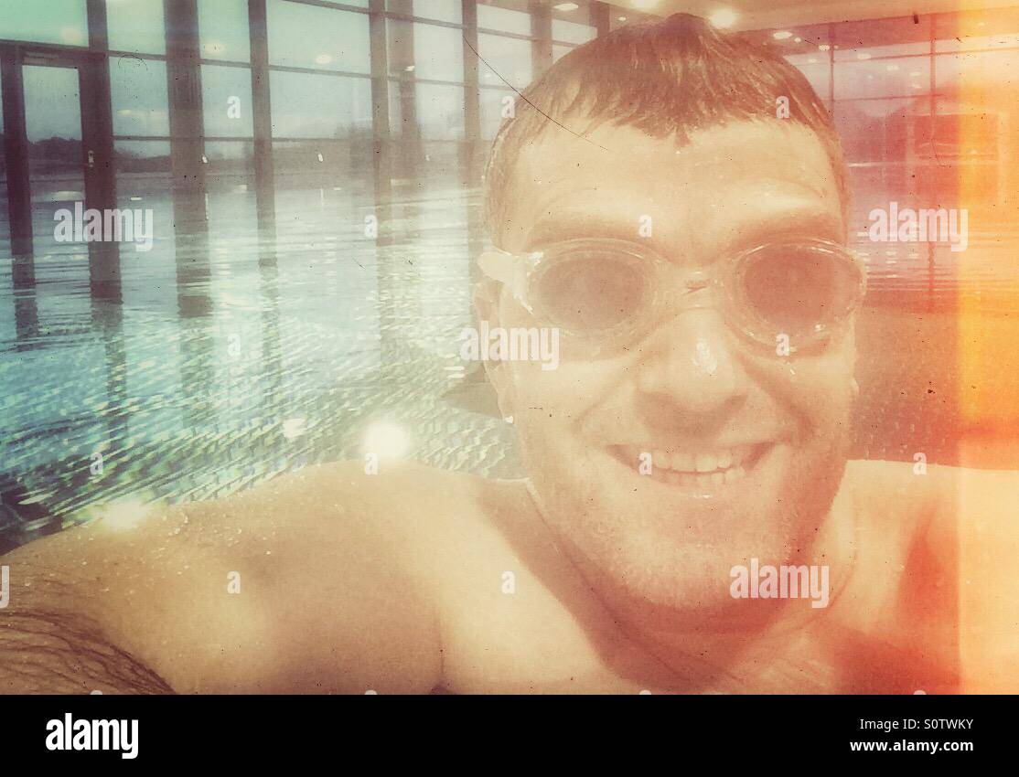 Jeune homme avec un bonnet de bain et lunettes posing in front of a  swimming pool and smiling Photo Stock - Alamy