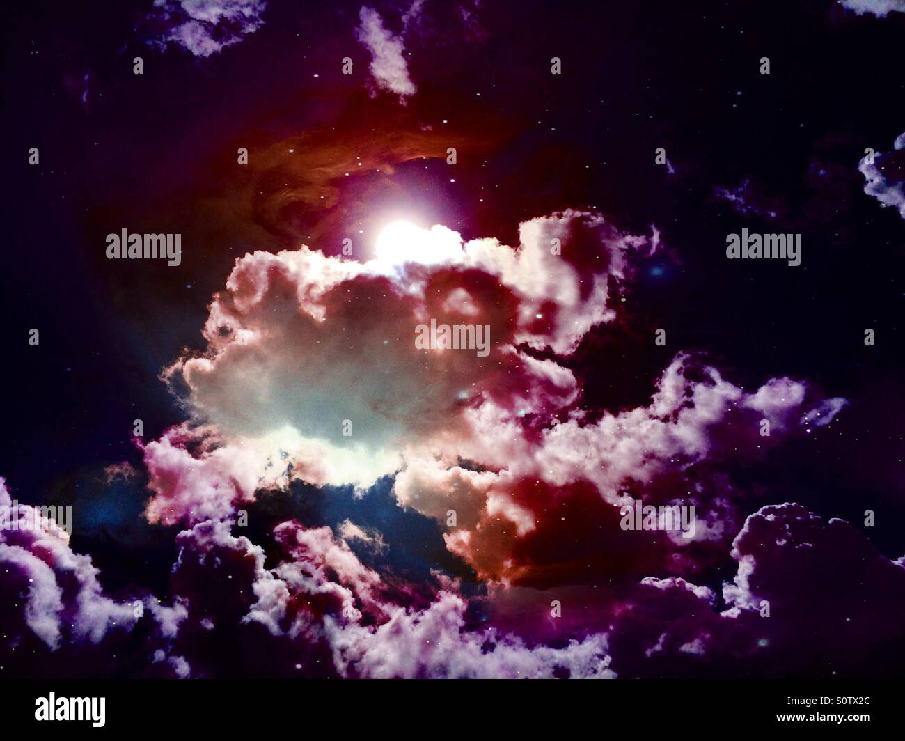 Dramatic purple sky with clouds and sun, with superimposed stars and nebulae Stock Photo