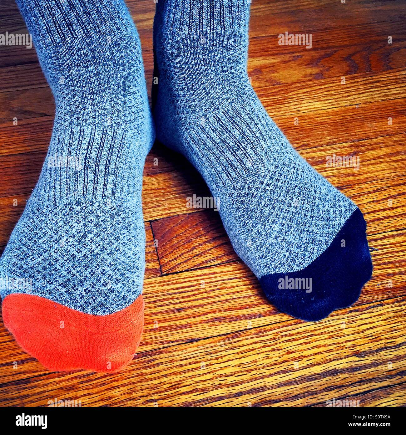 Man wearing mismatched gray socks with orange and blue toes on a