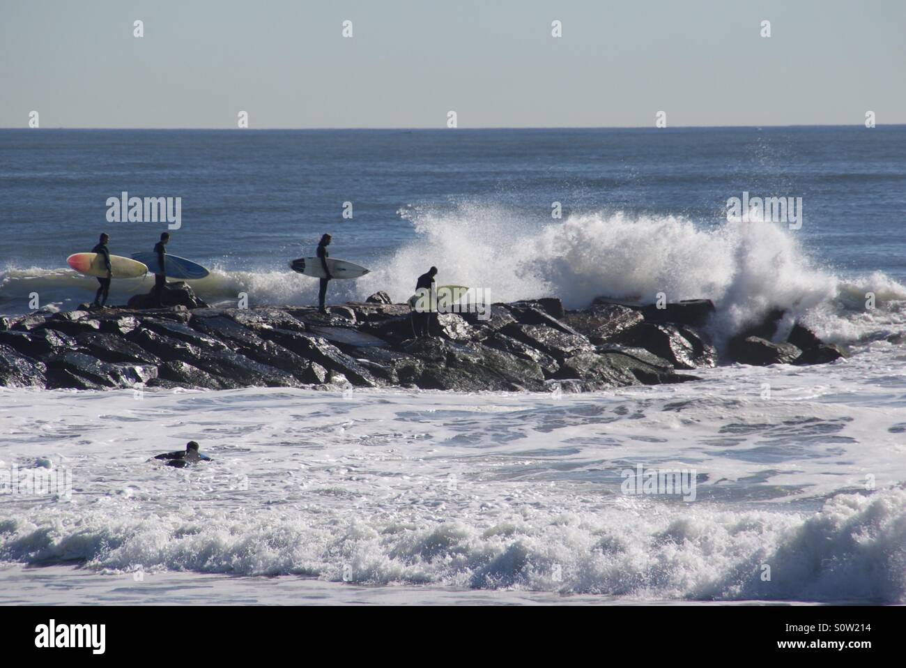 Surfers on a jetty with big waves, Rockaway beach, NYC Stock Photo
