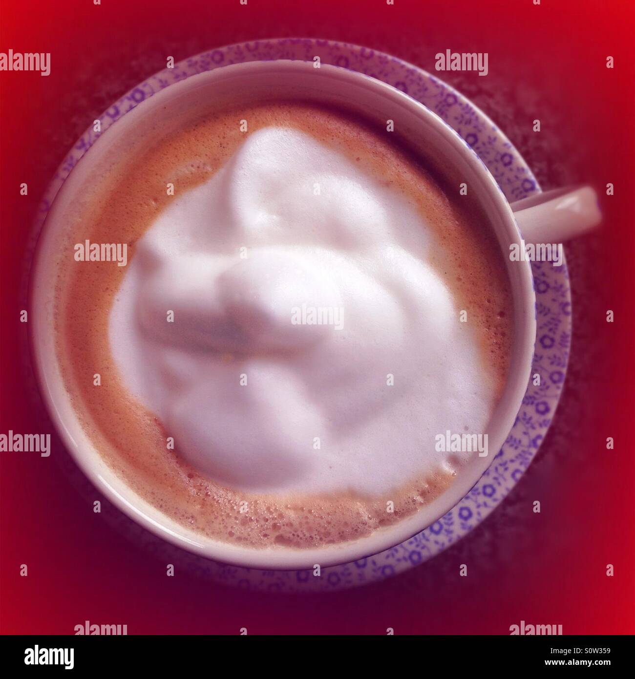 Latte coffee in blue cup and saucer, with red background Stock Photo