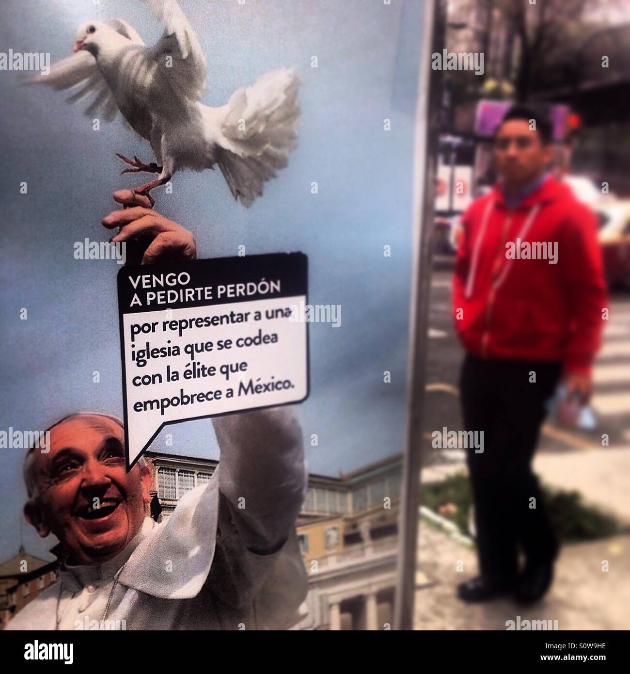 A sticker with a sign reading 'I come to apologize for representing a church that rub shoulders with the elite that impoverish Mexico' is pasted in a picture of the pope holding a white dove in Mexico - Smartphone Captured Stock Image