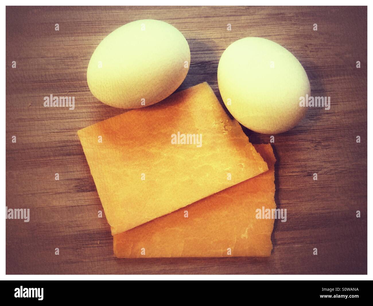 Eggs and cheese slices on a wood cutting board Stock Photo