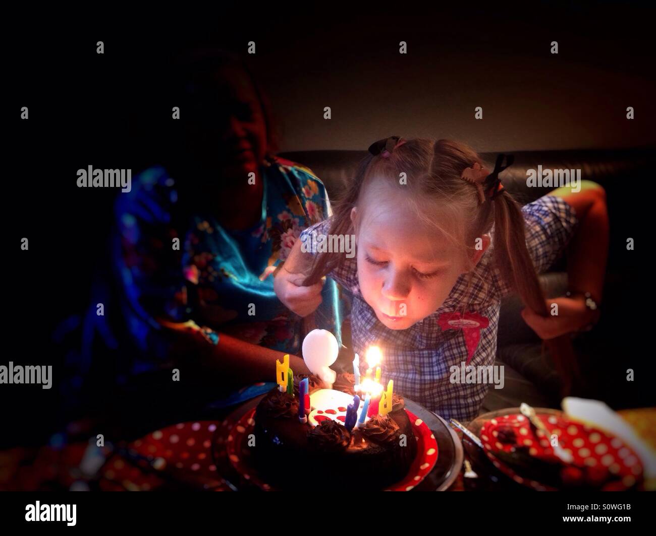Nine years old girl holding her piggy tails while blowing the candles on her birthday cake. - Smartphone Captured Stock Image
