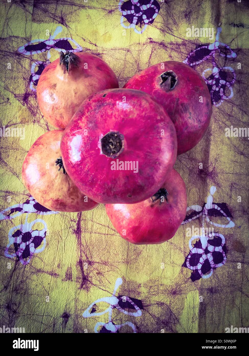 Five pomegranates artistically arranged on batik tablecloth. Harmonious colours. Wholesome, healthful, shiny. Symbolizing plenitude, beautiful nature. - Smartphone Captured Stock Image