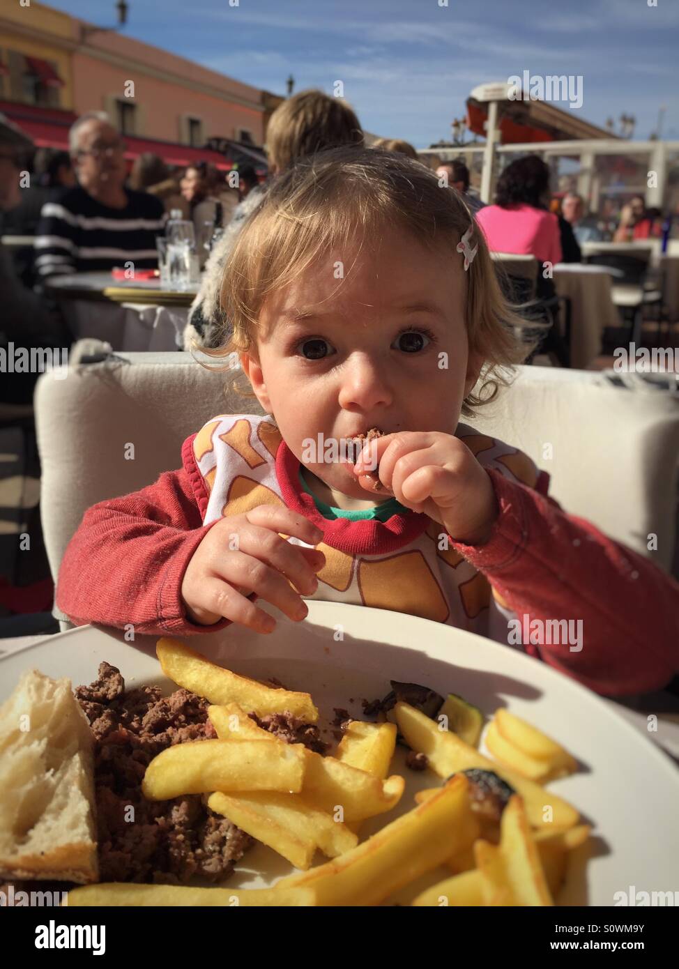 One year old baby eating French fries ands burger by herself Stock Photo