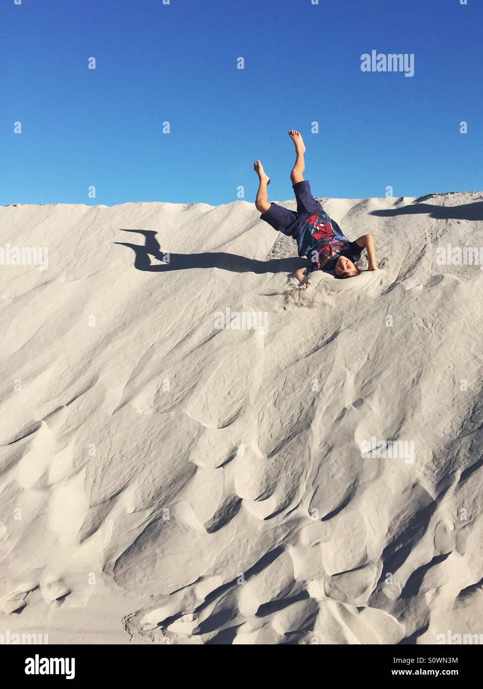 Boy rolling down a sand dune Stock Photo