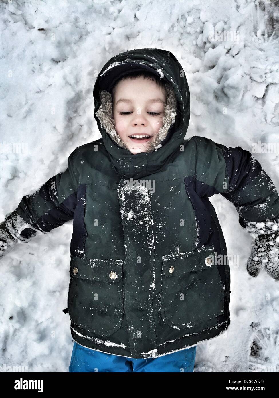 Young boy in a parka laying in the snow Stock Photo