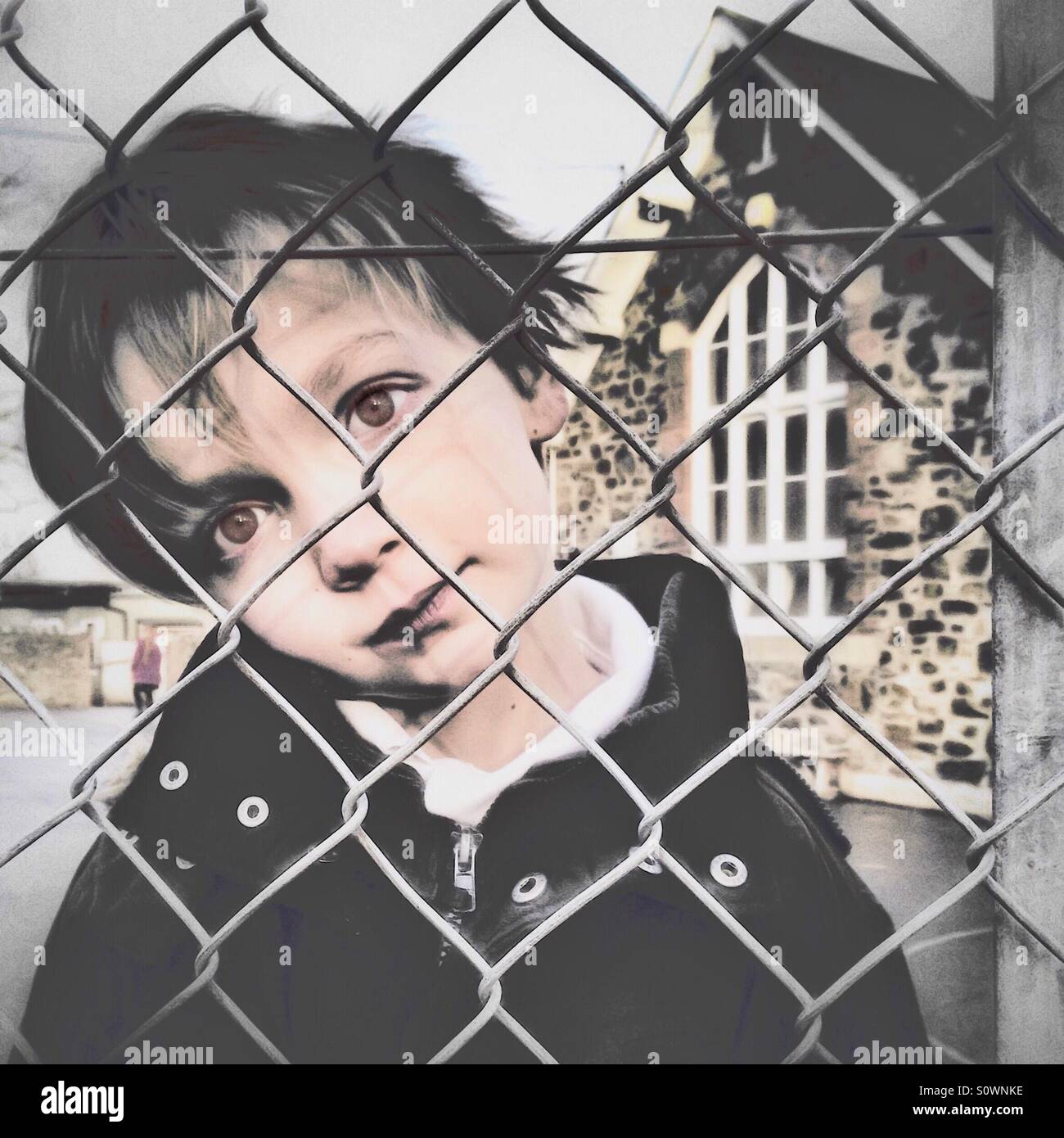Boy looking lost through school fence Stock Photo