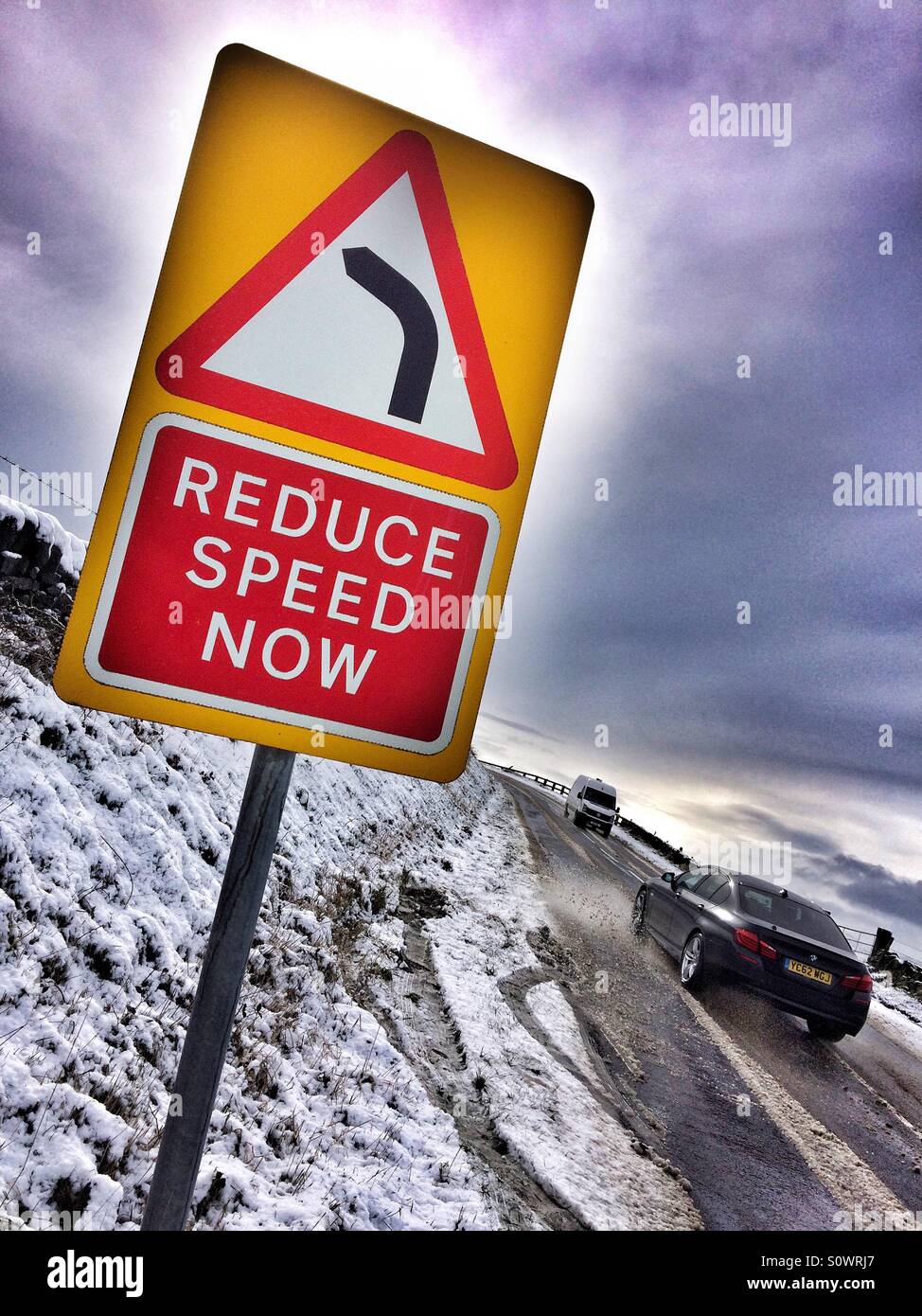 Driving in snow reduce speed bend ahead Stock Photo