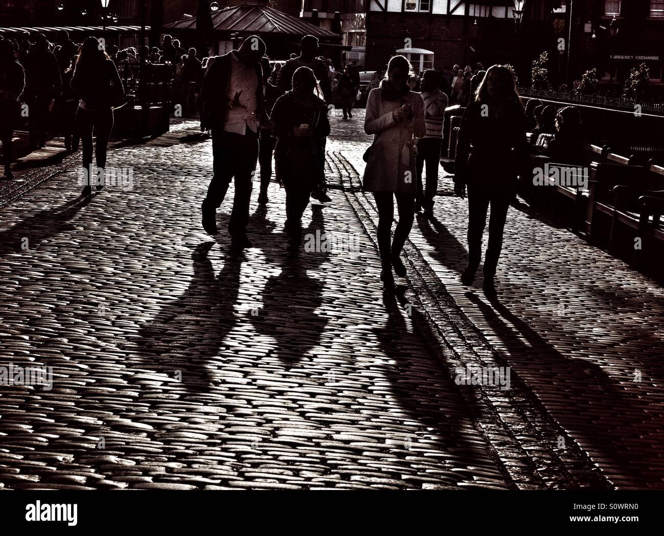 Young people stroll with their phones along a cobbled path beside the Thames in London, UK - Smartphone Captured Stock Image